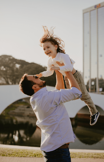 Pai em brincadeira jogando filha para cima enquanto ambos sorriem