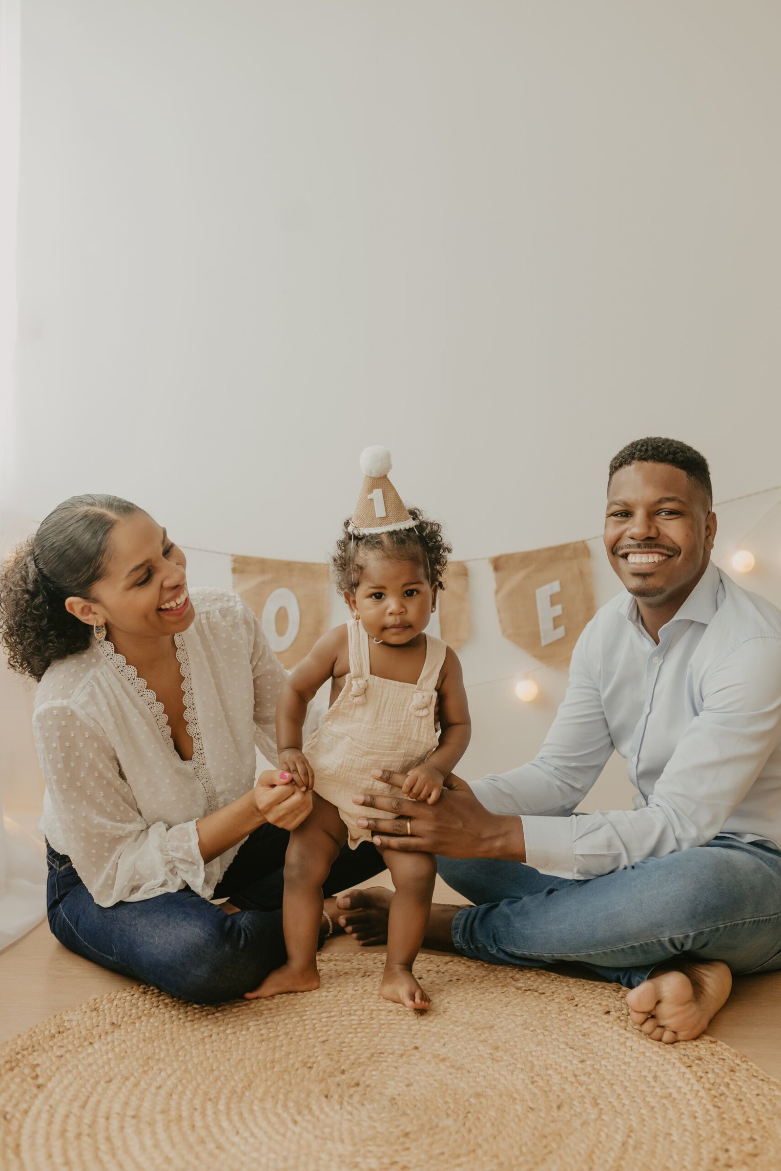 Mãe e Pai sentados no chão enquanto seguram sua filha no Ensaio fotográfico Smash The Cake