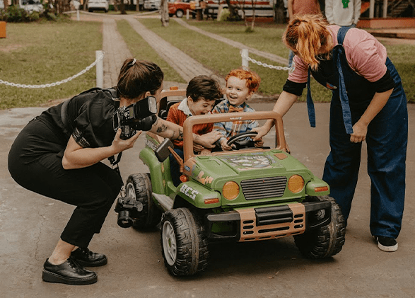 Duas crianças em jeep verde e fotógrafa interagindo com ambos.