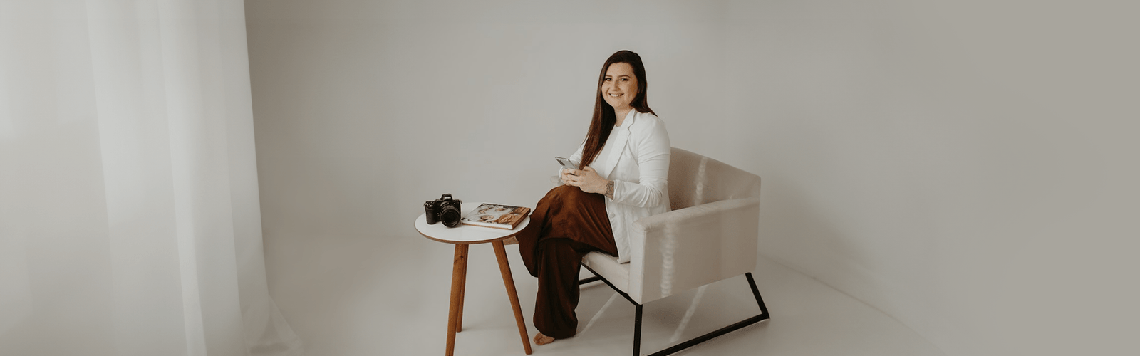 Fotógrafa Raquel Jesien sentada em uma poltrona minimalista em sala branco pastel